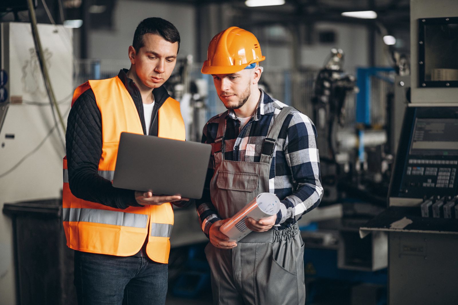 Dos trabajadores revisan información en un computador portátil dentro de una fábrica